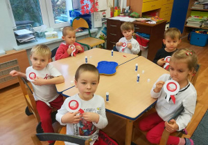 Szóstka dzieci przy stoliku prezentuje samodzielnie wykonane kokardy narodowe.